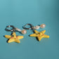 Pair of yellow star-shaped keychains with pearl-like beads on a teal background
