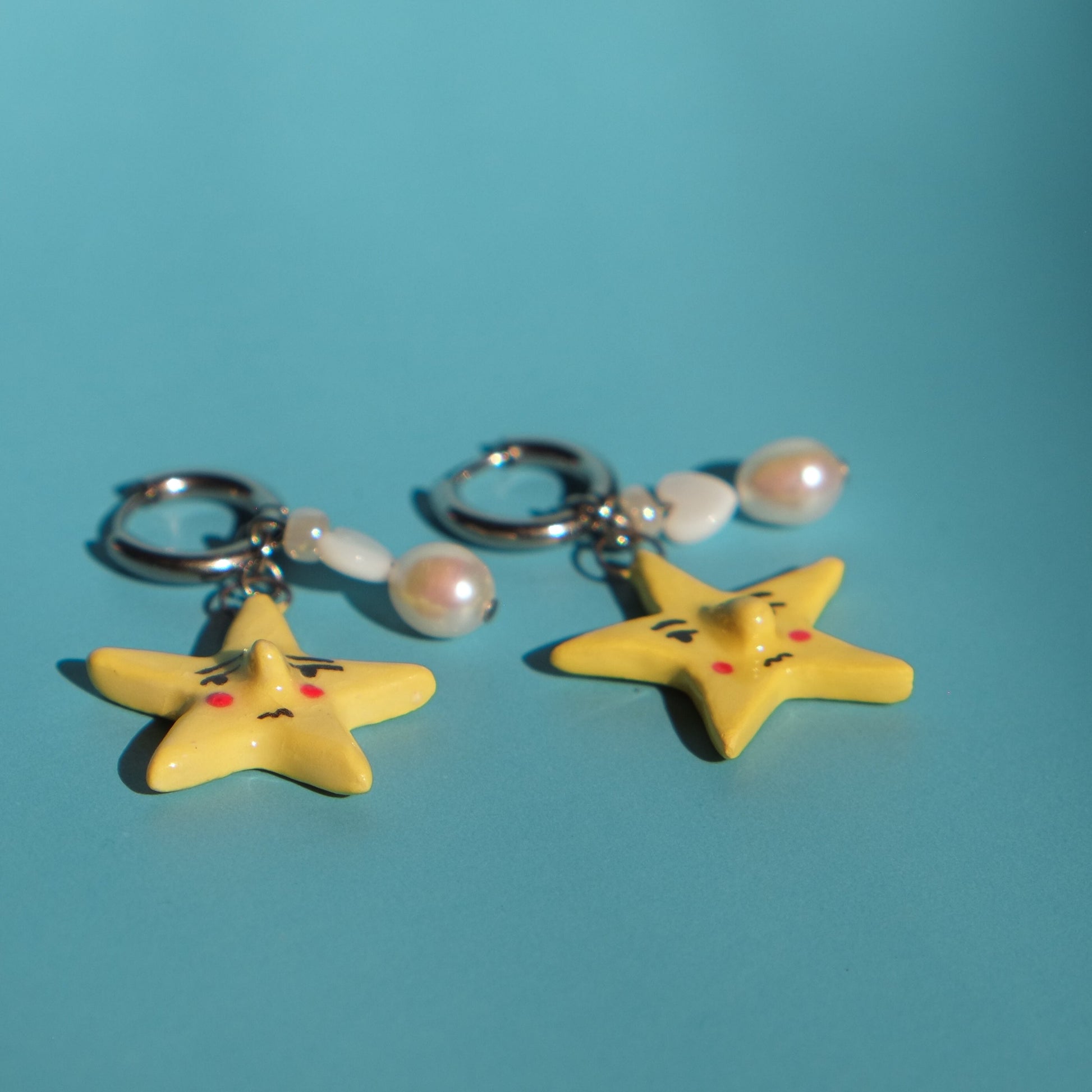 Pair of yellow star-shaped keychains with pearl-like beads on a teal background
